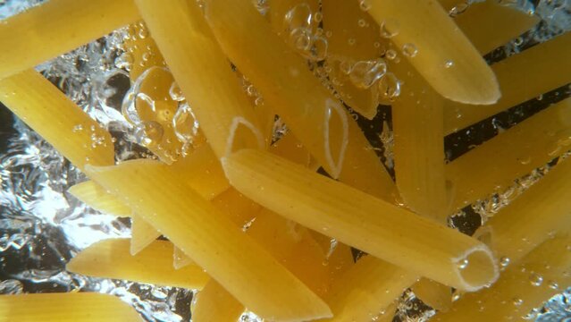 Super slow motion of falling uncooked italian pasta Penne into water, black background. Filmed on high speed cinema camera, 1000 fps.