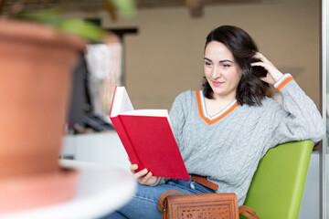 Young Caucasian woman enjoying reading a book. Hobbies and pastimes. Space for text.