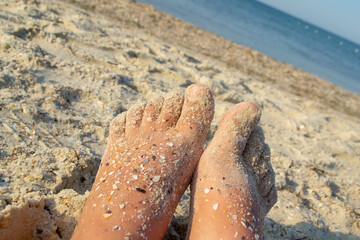 Fototapeta na wymiar Two bare feet of caucasian woman soiled in sand with shell rock on sandy sea shore on sunny summer day close-up. Relaxing on sea sandy beach. Concept of rest, relaxation, vacation, travel tourism