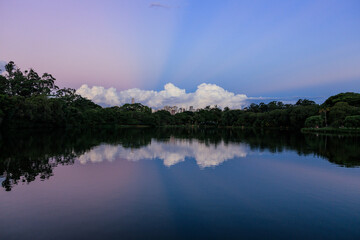Anoitecer em parque na cidade de São Paulo, com reflexo em lago nas cores azul e rosa.