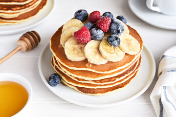 Stack of pancakes with berries and syrup on a kitchen table for breakfast. Good morning