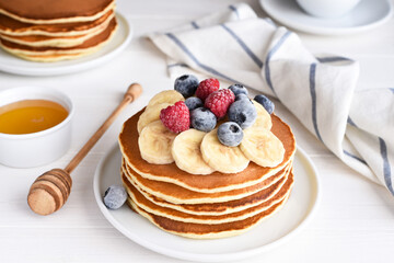 Stack of pancakes with berries and syrup on a kitchen table for breakfast. Good morning