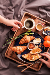 Couple eating continental breakfast from rustic wooden tray in bed - coffee and croissants
