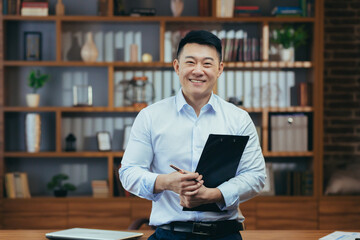 Portrait of a successful Asian teacher, a man in a shirt looking at the camera and smiling, in the...