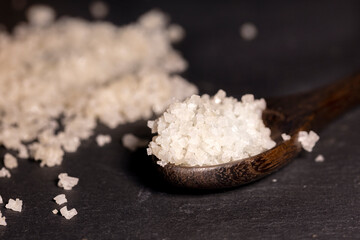 Wooden spoon holding  white sea salt crystals on a black slate cutting board