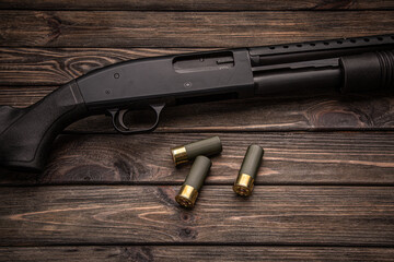 A black 12-gauge pump-action shotgun and ammo are on a wooden table. A smooth-bore weapon with a...