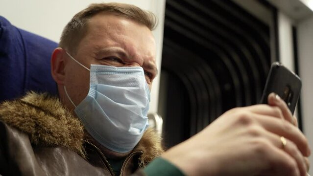 Disgusted and overwhelmed cringe millennial man stares at screen of smart phone while riding home by train passes through suburbs during Covid-19 or coronavirus pandemiсбб new normal