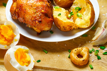 tasty and healthy food, lunch in rural style - fried chicken meat and unpeeled potatoes, eggs, green leek, salt and garlic, cooked food on a wooden kitchen board