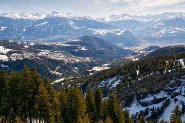 Switzerland, Wallis.  Alps mountains  in a haze covered with snow  in Switzerland in winter
and trees in the foreground.