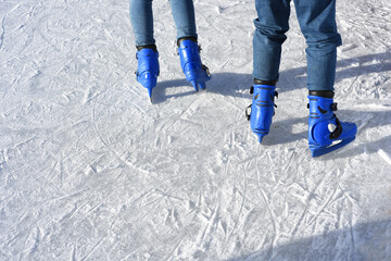 Fototapeta na wymiar Feet of the two skaters in blue boots on skates on ice rink. Winter time, outdoor activities. Sunny day. Text space.