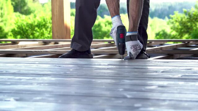 A man screws a wooden terrace on a sunny day