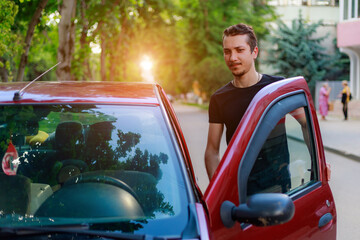 A young man or adult guy driver gets into the car. Background with copy space