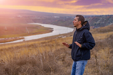 man tourist or a hiker in a windbreaker is engaged in spiritual practices at dawn. Background with...