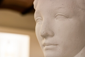 Classic bust of a sculpture made with plaster with some lights at the background with a nice warm tone and copy space. Neutral tones.