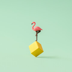 Creative layout made of pink flamingo standing on top of the yellow cube against pastel green background. Minimal spring or summer pop art concept.
