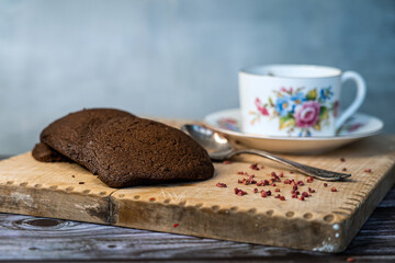 A cup of black tea with chocolate cookies on a wooden plate
