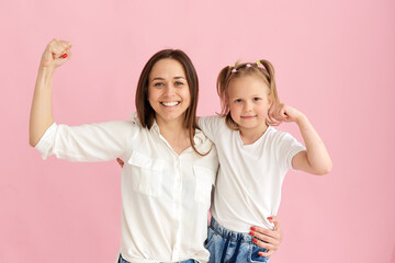 Mom and daughter show their muscles and strength in the studio on a pink background
