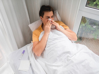 Sick man is lying in bed with thermometer. Man is blowing his nose. Temporary disability in case of...