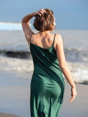 Fototapeta na wymiar Caucasian woman in green silk dress. Pretty woman at seaside. Long-awaited vacation. Golden star temporary tattoo. View from the back.