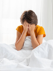 Sleepy woman is sitting in bed, completely covered with white blanket. It's hard to wake up early in morning. Woman does not get enough sleep.