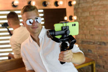 A European young guy is reflected in the mirror with a tripod and a phone. Blogger generates content for his social media page