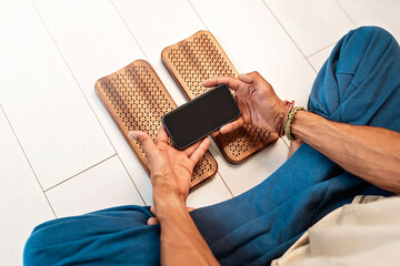 Practice of standing on nails. Man sitting in lotus position with phone on a light background....