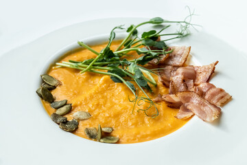 Creamy pumpkin soup with toasted bacon pieces garnished with pumpkin seeds. Healthy low-calorie soup in a white plate