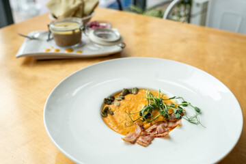 Creamy pumpkin soup with toasted bacon pieces garnished with pumpkin seeds. Healthy low-calorie soup in a white plate on a wooden table in a cafe