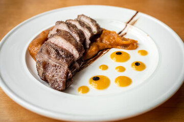 Roast duck cut into pieces served with pumpkin sauce on a plate. Diet duck on a wooden table in a cafe