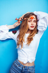 young pretty blond girl posing on blue background, fashion style hippie boho flowers on head