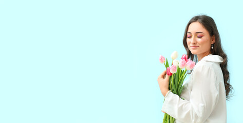 Obraz na płótnie Canvas Happy young woman with creative makeup holding bouquet of tulips on blue background with space for text. International Women's Day