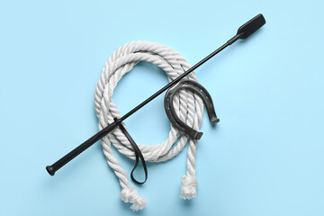 Horse riding crop with rope and horseshoe on color background