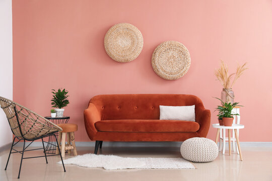 Stylish orange sofa with houseplants and wicker armchair in modern interior of living room
