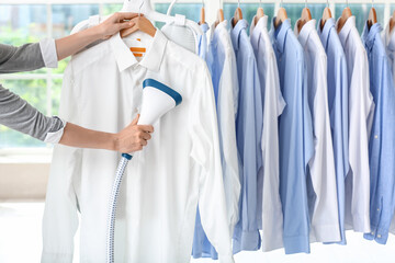 Woman ironing shirt with steam at dry-cleaning - obrazy, fototapety, plakaty