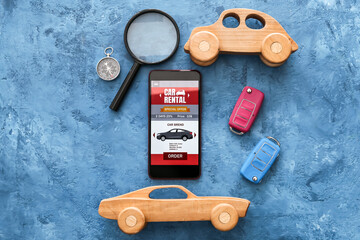 Mobile phone with open car rent app, toys, keys, magnifier and compass on grunge background