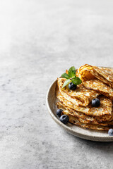 Delicious homemade crepes on ceramic plate with blueberry and mint on gray background for maslenitsa