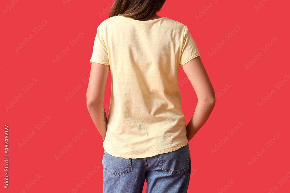 Wall mural Young woman in blank t-shirt on color background, back view