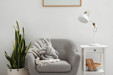 Stylish lamp on table, armchair and houseplant near light wall