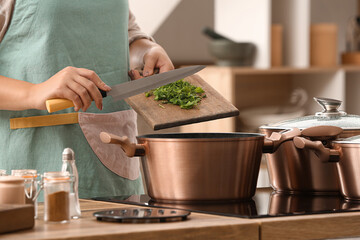 Woman adding greenery into cooking pot in kitchen, closeup