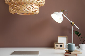 Modern workplace with laptop and lamps near brown wall