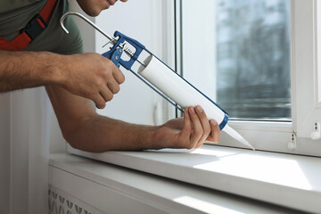 Construction worker sealing window with caulk indoors, closeup