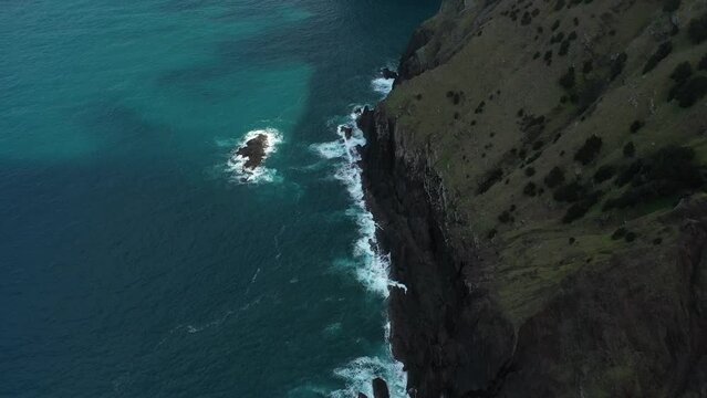 Drone shot of the cliff side of Espigao Amorelo in Madeira with its dramatic and steep cliff. Dark blue and turquoise water with reefs below as the waves crashes against the rocks.