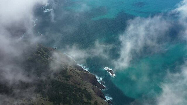 Drone shot of the cliff side of Espigao Amorelo in Madeira moving down through the thin clouds and tilting downwards to reveal the cliffside and colorful ocean.