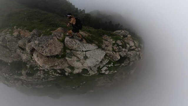 A young and fit solo hiker is jumping between rocks on the edge of the steep cliff of Espigao Amorelo in Madeira, surrounded by mist, fog and clouds. A risky and dangerous act full of adrenaline.