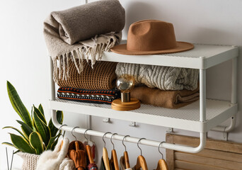 Rack with stylish knitted sweaters, felt hat and scarf near light wall