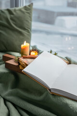 Opened book with blank pages, burning candles and winter decor on windowsill