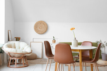 Vase with beautiful Gerbera flower on dining table and comfortable pouf in room