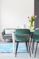 Dining table with stylish setting and vase with tulips in room
