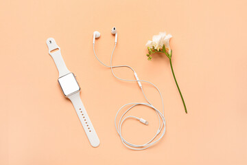 Smart watch, earphones and flower on color background