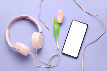 Mobile phone, headphones and tulip flower on color background